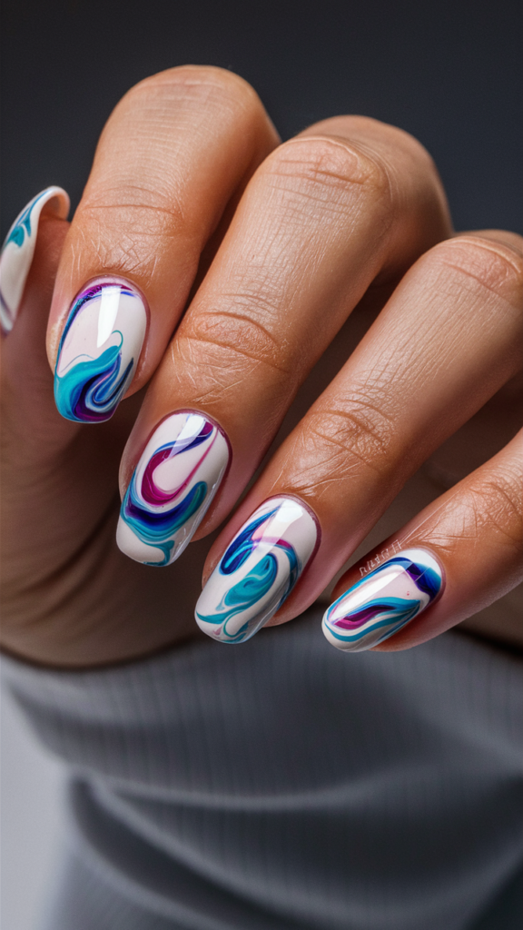 Image of nails with a vibrant tie-dye pattern in colors like blue, purple, and pink. The colors swirl together smoothly, creating a blended, retro-inspired effect that captures the laid-back vibe of streetwear tie-dye. Each nail showcases a unique variation of the tie-dye pattern, with the colors fading seamlessly into one another. The design is playful and colorful, offering a fun and nostalgic nod to the tie-dye trend that has made a major comeback in modern street fashion.