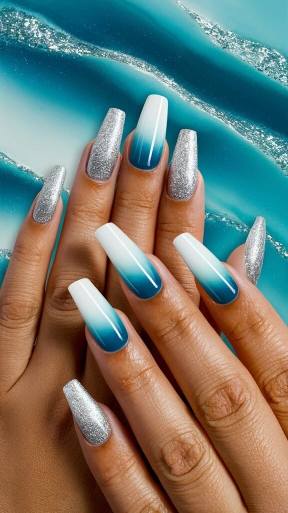 A close-up of nails featuring a gradient from deep ocean blue at the tips to soft sky blue at the base, adorned with realistic white wave patterns cresting over the tips. Silver glitter subtly accents the design, reflecting light like sunlight on water. The overall look captures the serene and dynamic essence of the ocean, with a glossy finish that enhances the vibrant colors and intricate details of the waves.