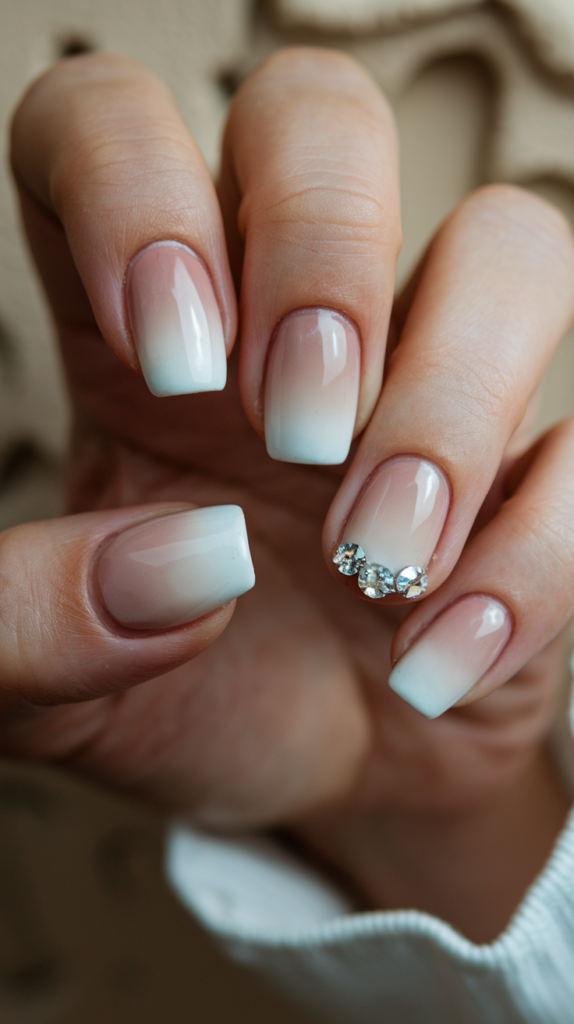 French ombré acrylic nails with a soft gradient from nude to white, adorned with rhinestone accents for added sparkle and subtle glam.

