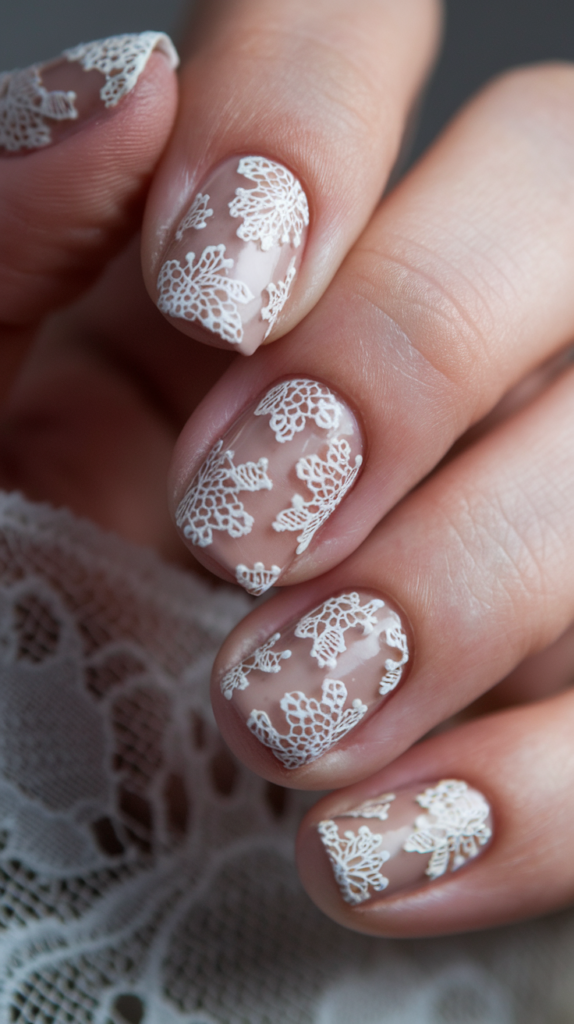 Nails with delicate lace-like floral patterns painted in white on a nude background, creating an elegant, intricate lace effect