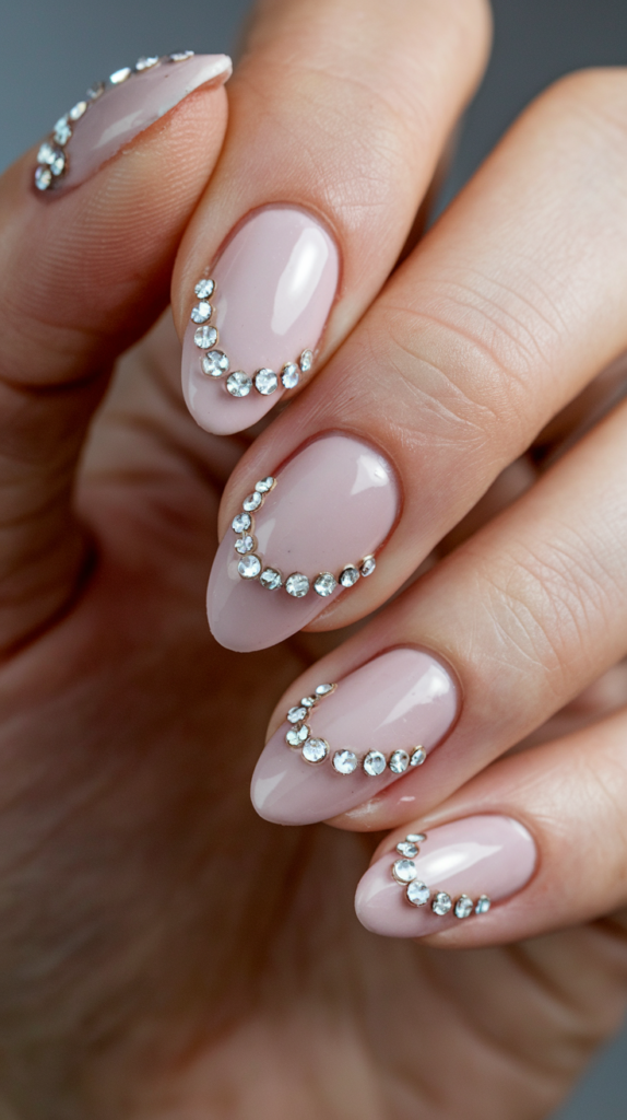 Light pink nails with sparkling rhinestones strategically placed for a glamorous, jewel-like effect