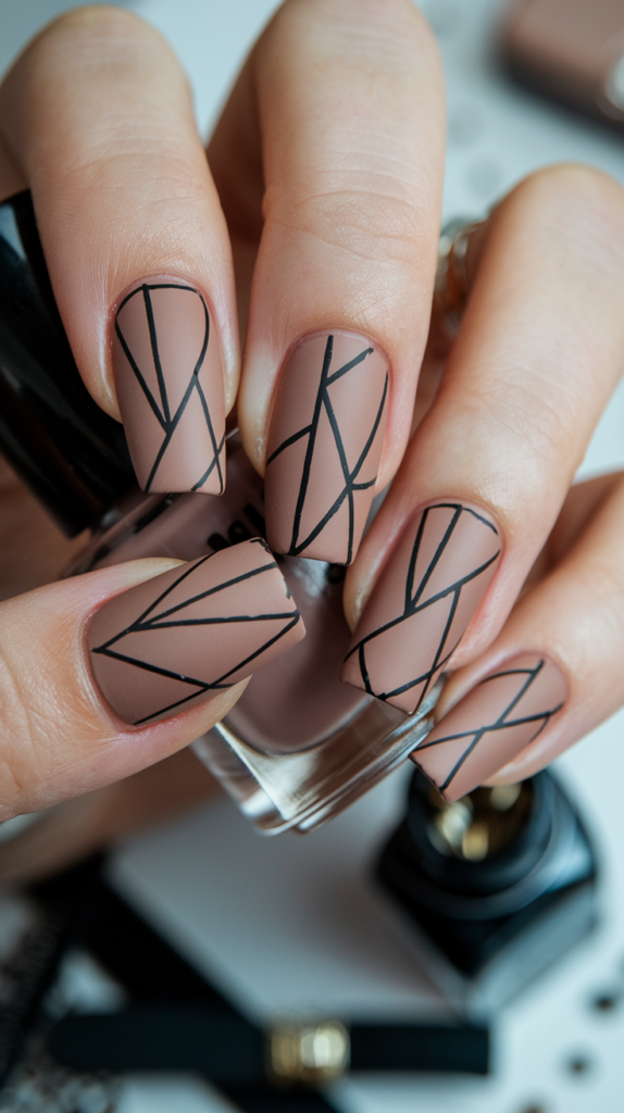 Matte nude acrylic nails with sharp black geometric shapes, creating a modern and minimalistic design that’s sleek and sophisticated.