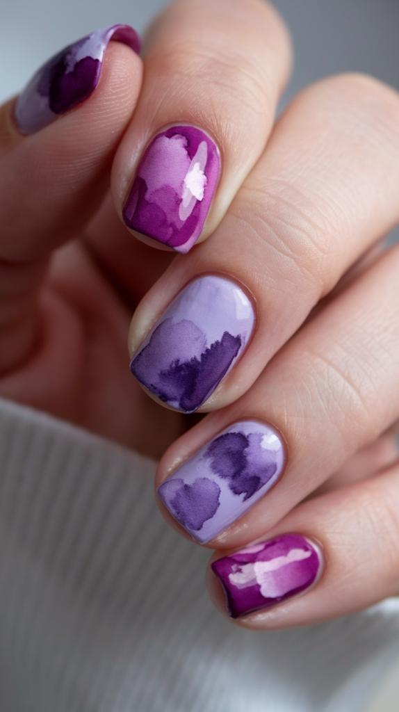 Abstract watercolor-style nails using various purple tones, creating a soft, artistic effect.
