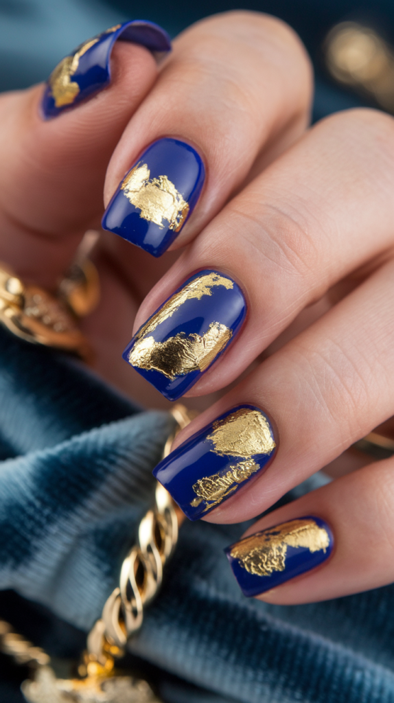 Bold cobalt blue nails adorned with irregular gold leaf accents, adding a luxurious and artistic touch