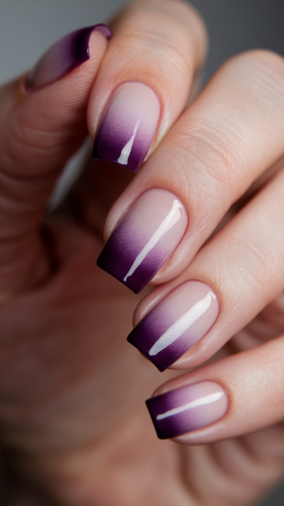 French fade nails transitioning from deep violet tips to a soft, nude base in a gradient.