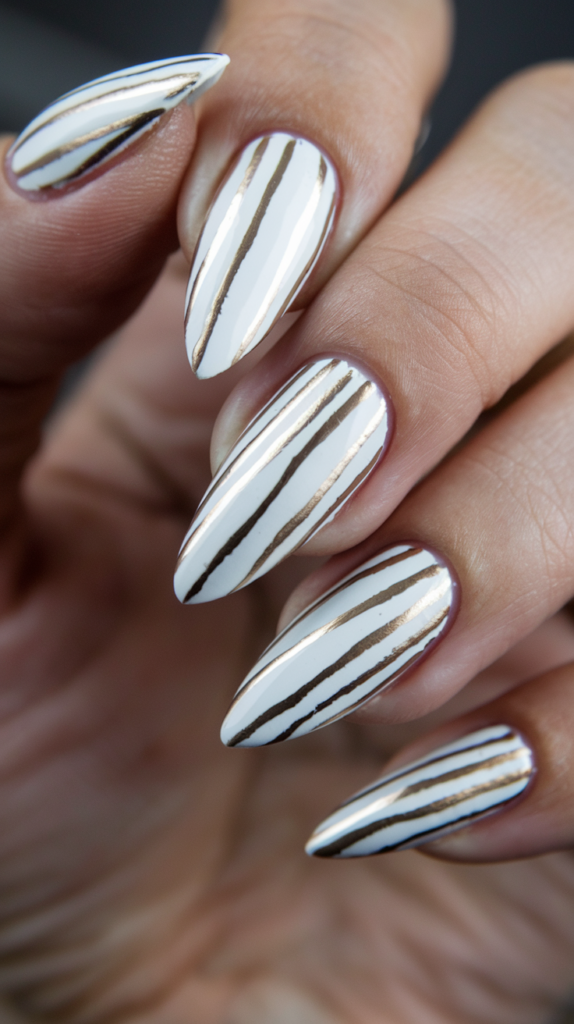 Sharp white stiletto nails accented with thin gold stripes.
