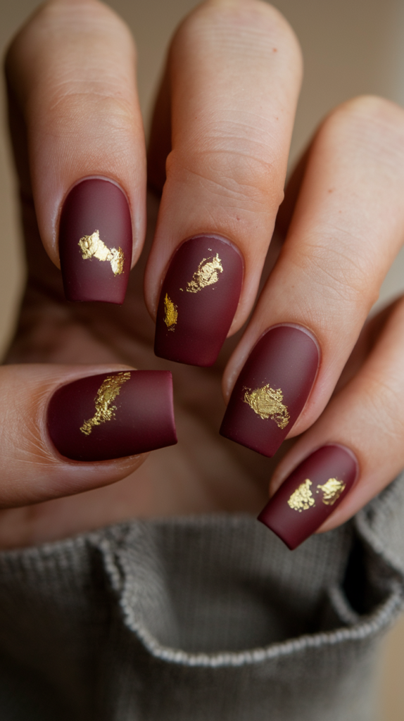 Rich matte burgundy nails with delicate gold leaf accents, showcasing a luxurious and timeless design perfect for formal occasions.

