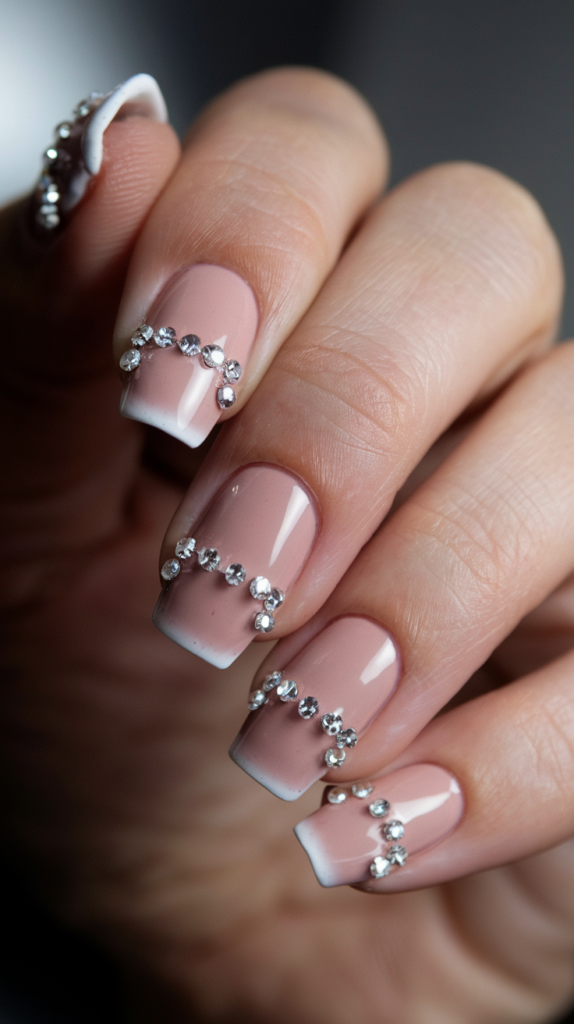 Nude base nails with diamond-like rhinestones forming sparkling French tips.
