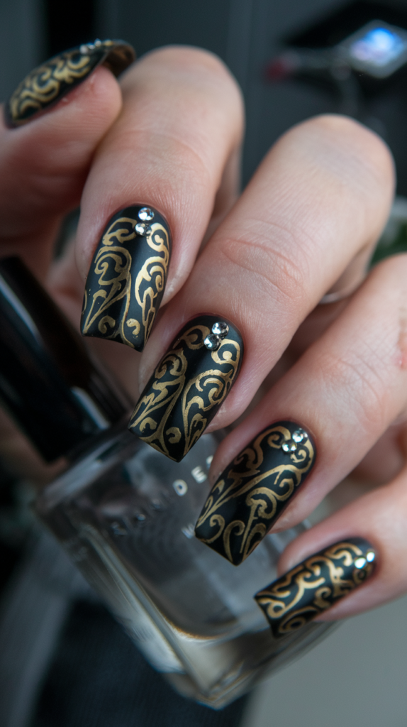 Nails with black base and swirling gold filigree patterns, embellished with rhinestones.

