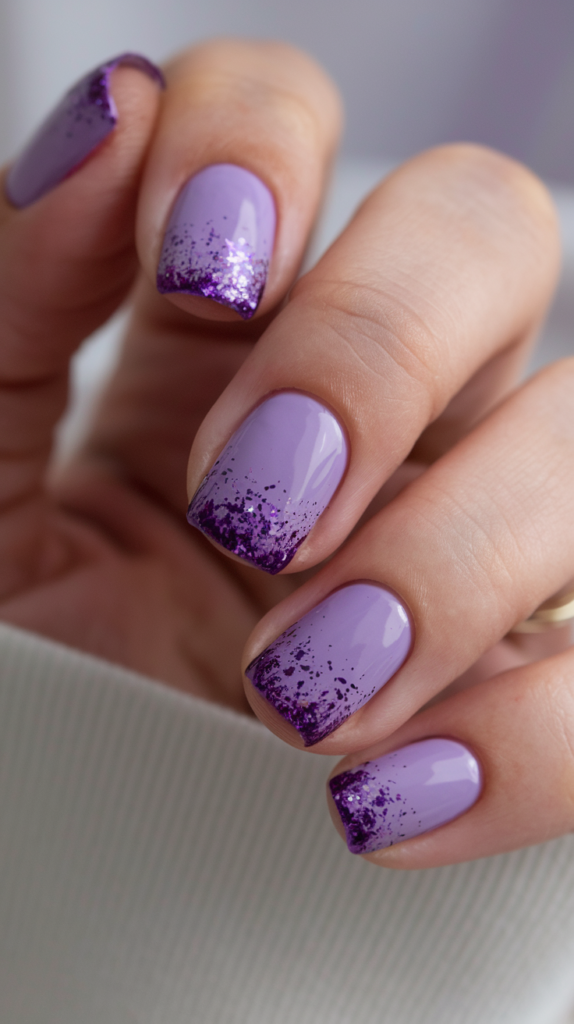 Nails with a deep violet base, adorned with a gradient of violet glitter fading from the tips, adding a sparkling effect.

