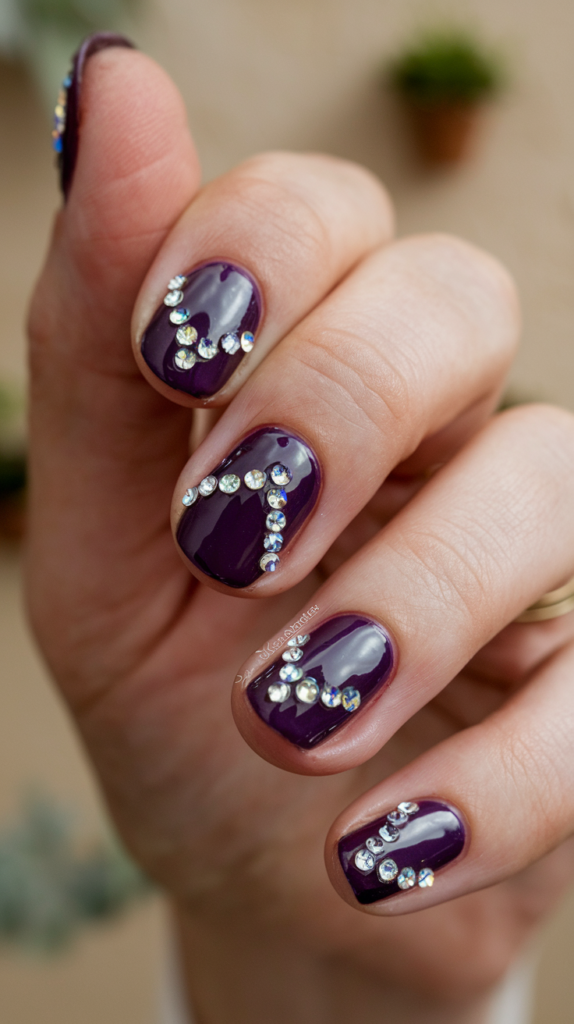 Deep violet nails adorned with small crystal embellishments for a glamorous, sparkling appearance.

