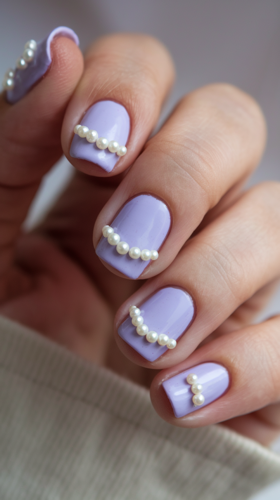 Pastel violet nails adorned with small pearl accents near the cuticle for a refined, elegant style.

