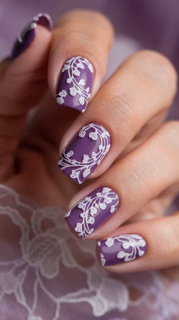 Dark violet nails with delicate white lace patterns painted over, offering a vintage-inspired, feminine look.

