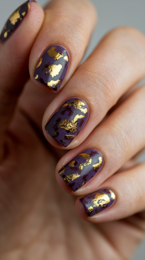 Dark violet nails highlighted with flecks of gold foil scattered across the surface for a royal, luxurious appearance.

