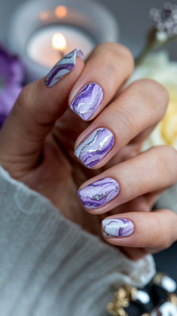 Marbled nail design featuring different shades of violet intertwined with white and silver veins, resembling polished stone.

